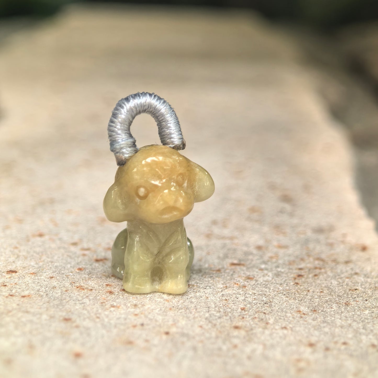 Natural Grade-A glutinous light yellow puppy jadeite charm shown standing on stone background.
