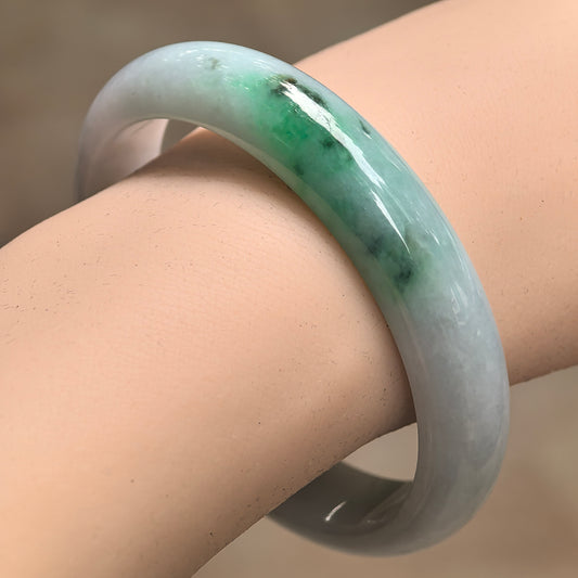Natural Grade-A glutinous green-white D-shape jadeite bangle worn on wrist with vivid green accent.
