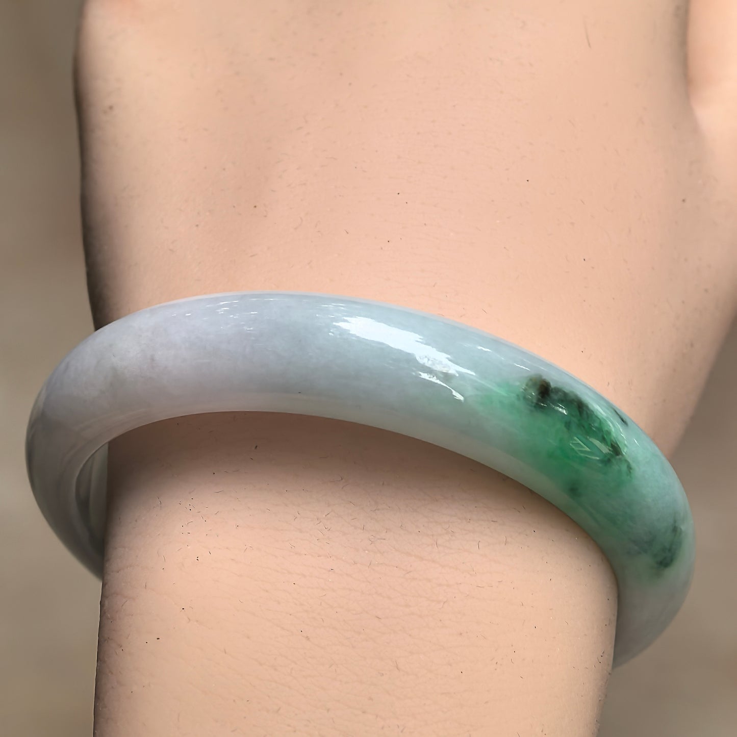 Close-up of green-white jadeite bangle showing polished luster and natural green color section.
