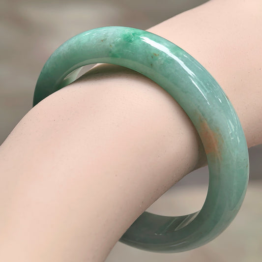 Natural Grade-A glutinous green golden-flecked D-shape jadeite bangle worn on wrist with glossy luster.
