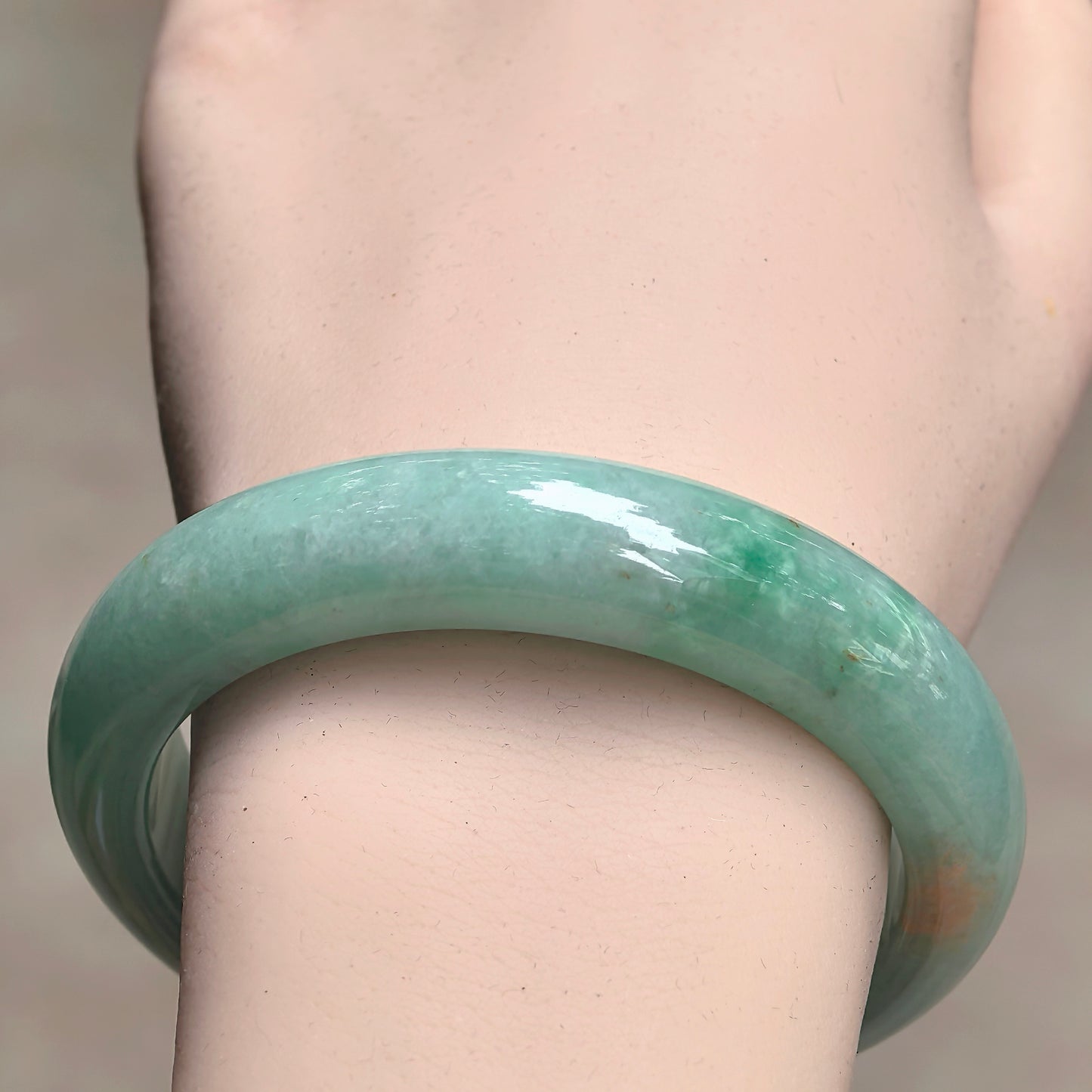 Close-up of full green jadeite bangle showing golden-yellow flecks and smooth polished surface.
