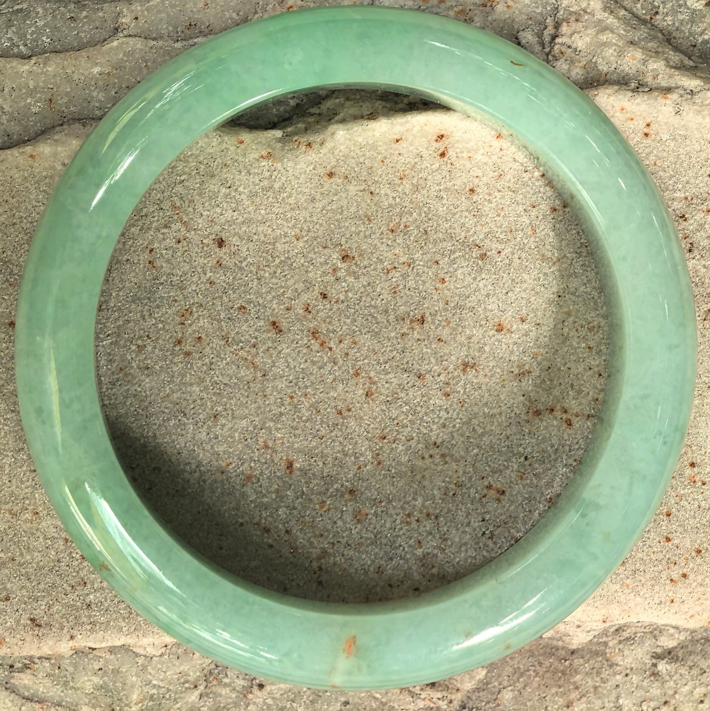 Top view of green jadeite bangle with natural golden-yellow flecks and rounded outer profile.
