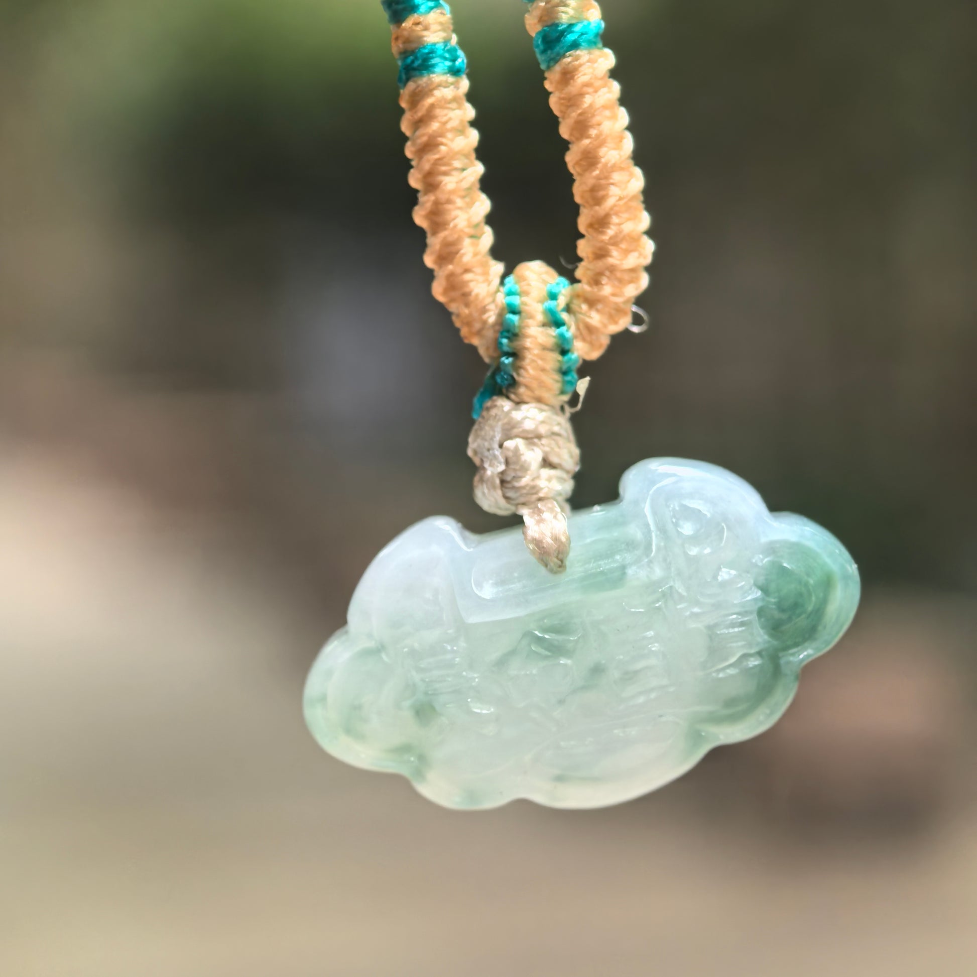 Natural Grade-A glutinous light green cloud lock jadeite pendant hanging on woven cord.