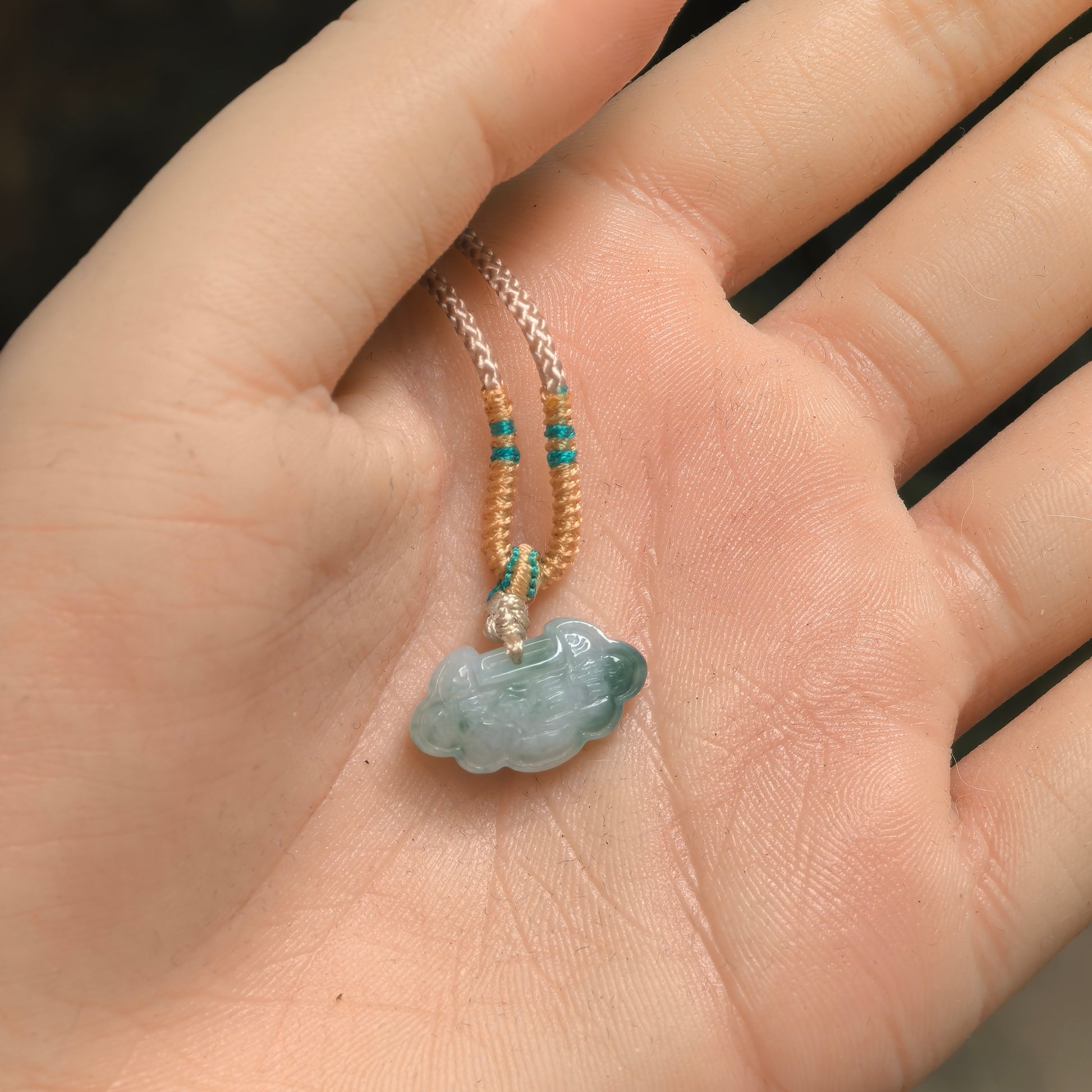 Petite light green jadeite cloud lock pendant shown in hand for scale.
