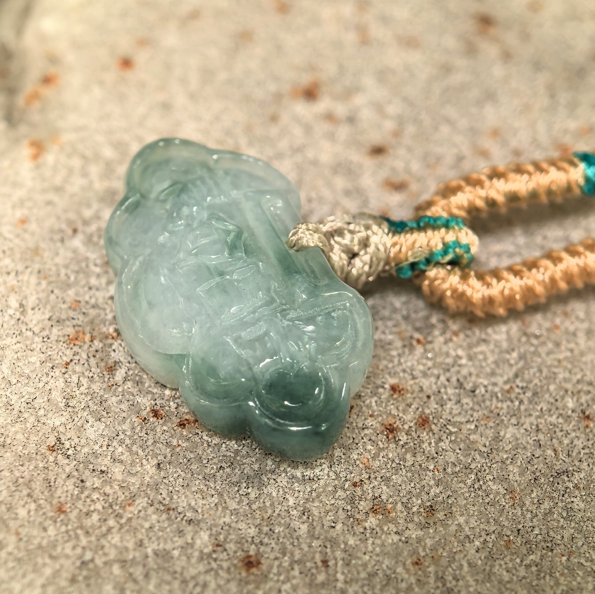 Side view of small light green jadeite pendant showing compact thickness and smooth polish.
