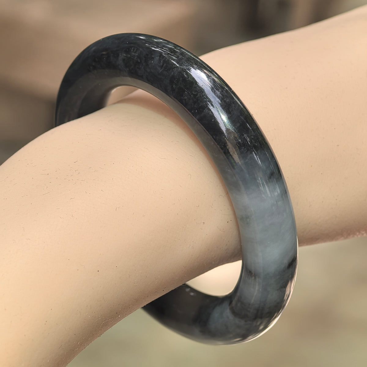 Natural Grade-A glutinous black-gray round jadeite bangle worn on wrist with smoky color variation.
