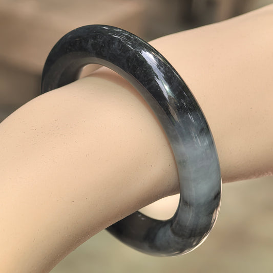 Natural Grade-A glutinous black-gray round jadeite bangle worn on wrist with smoky color variation.
