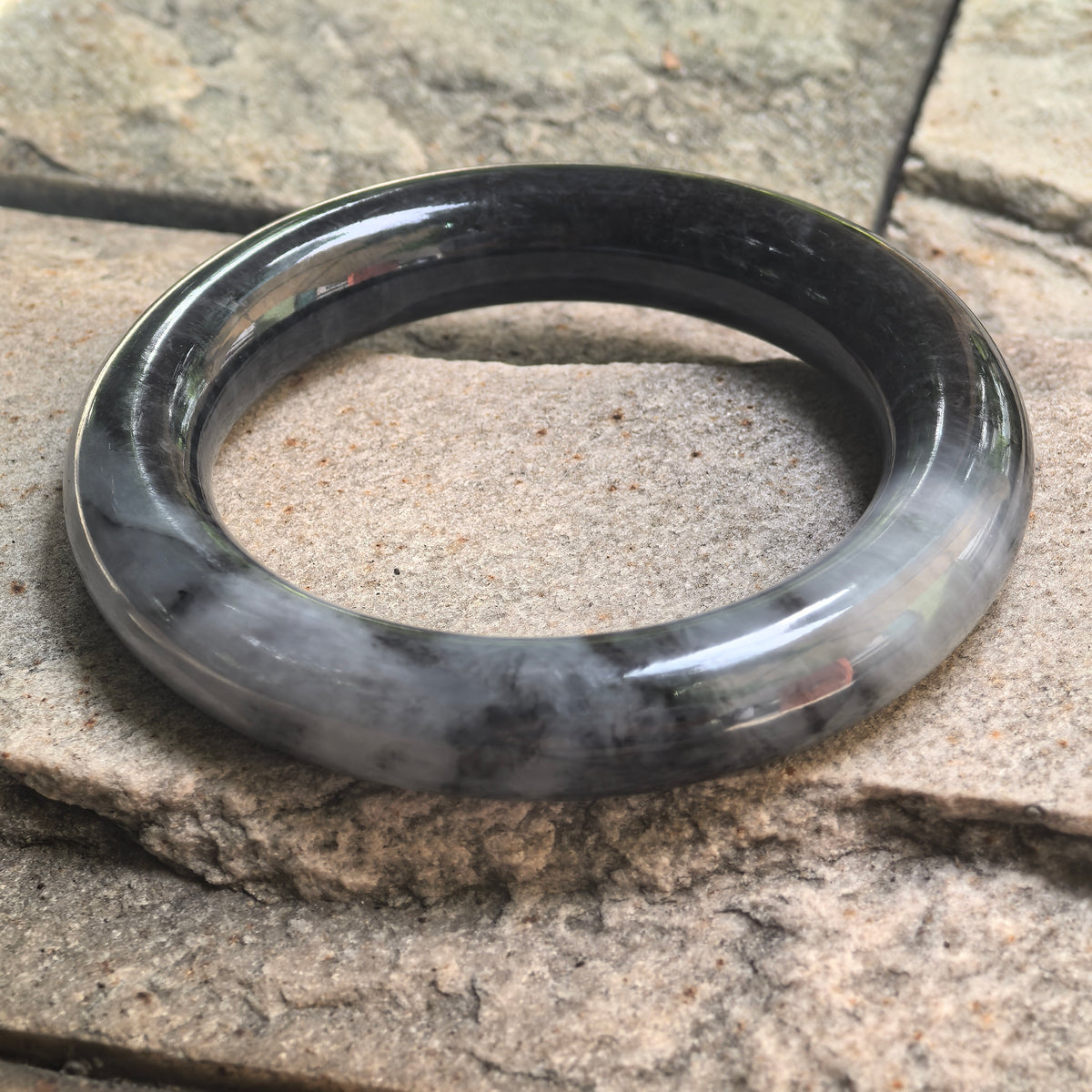 Natural Grade-A smoky gray jadeite round-bar bangle displayed on stone background.
