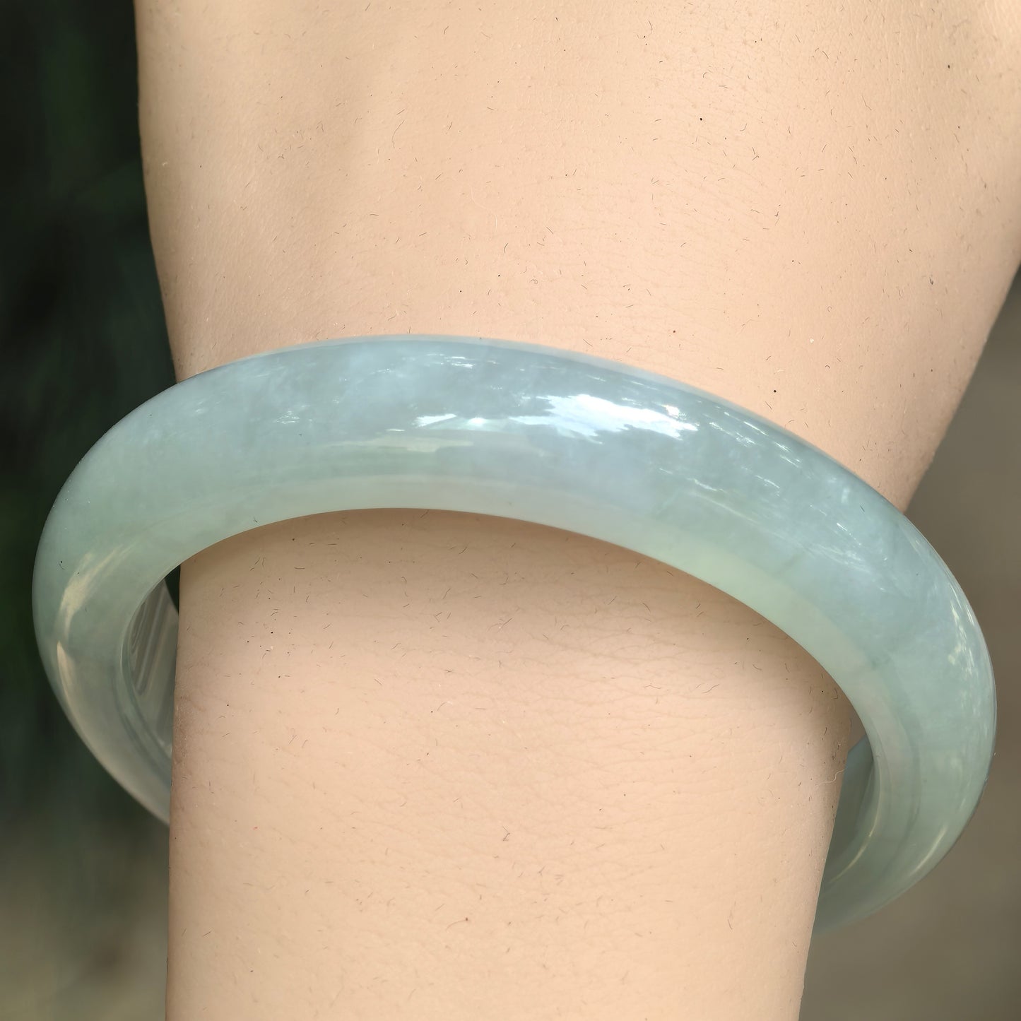 Close-up wrist view of a mint green Burmese jadeite bangle with good translucency and soft natural texture.