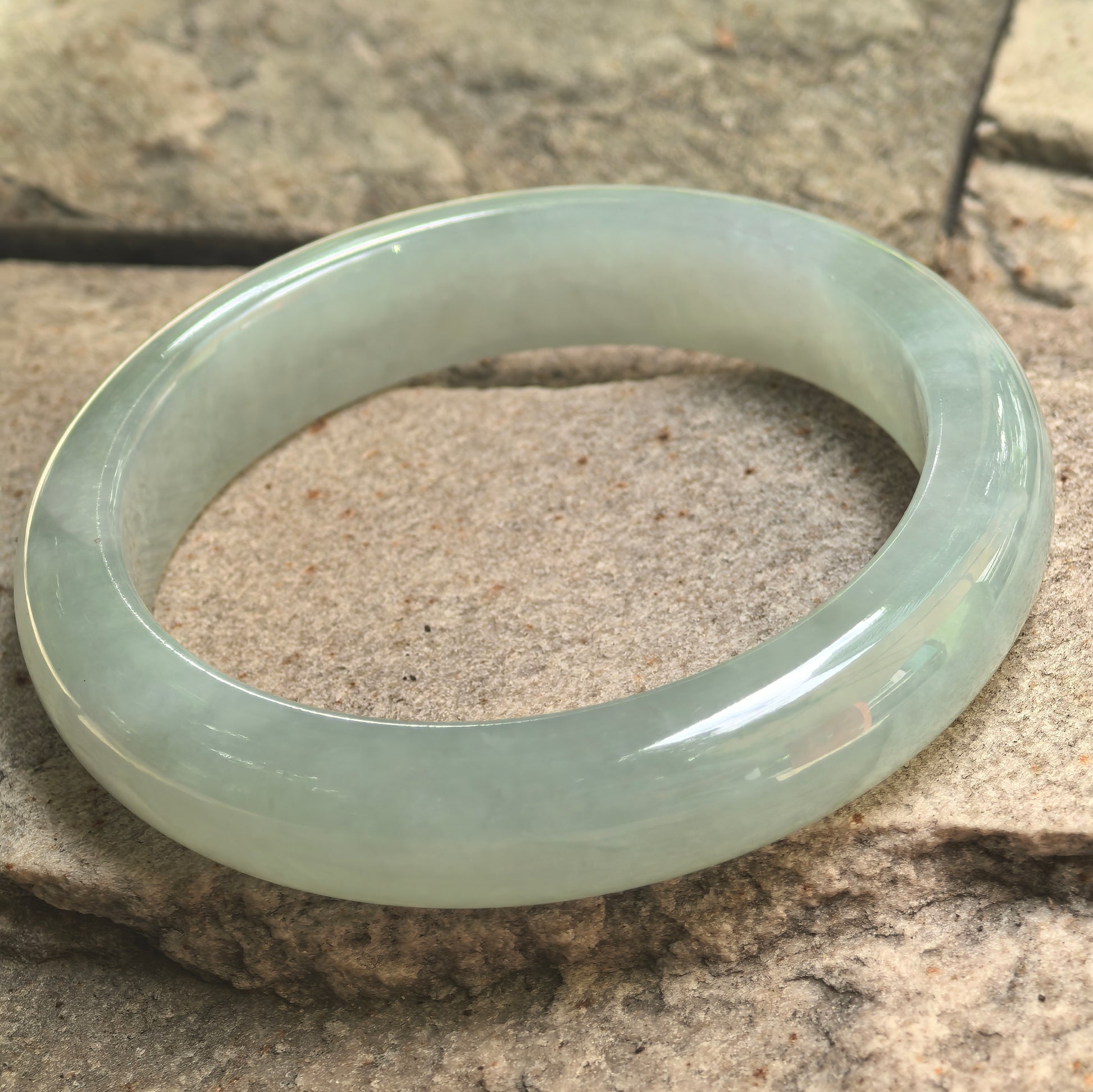 Icy glutinous mint green jadeite bangle displayed on stone, showing its broad profile and glossy surface.