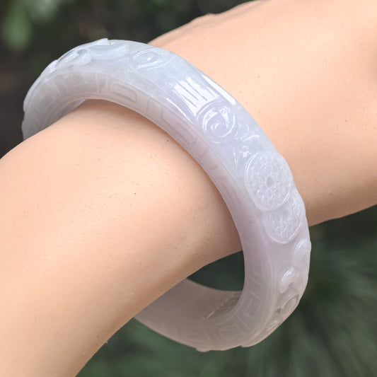 Glutinous white jadeite bangle worn on wrist showing carved floral and geometric details.
