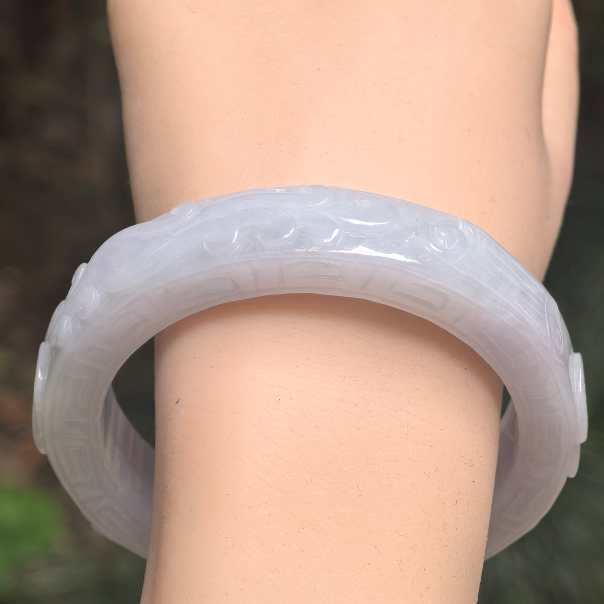 Close-up of white carved jadeite bangle with soft luster and natural circular lines.
