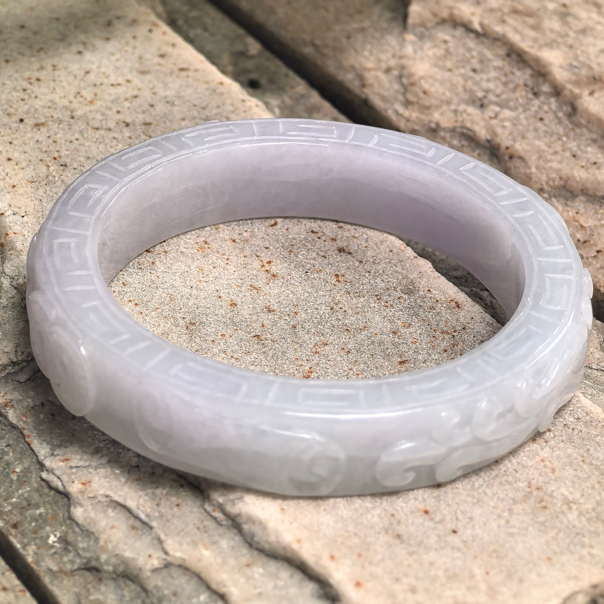 Natural Grade-A Burmese jadeite bangle displayed on stone background with traditional carved design.
