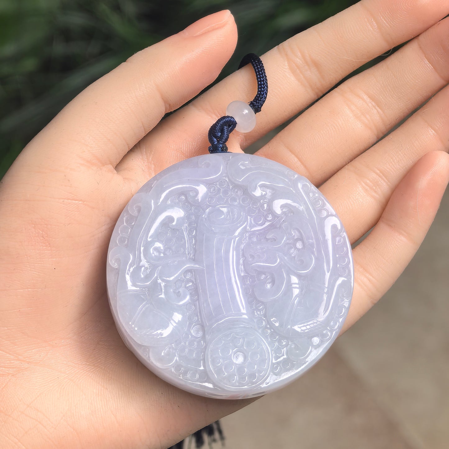 Large round white jadeite ornament shown in hand with raised decorative carving and soft translucency.
