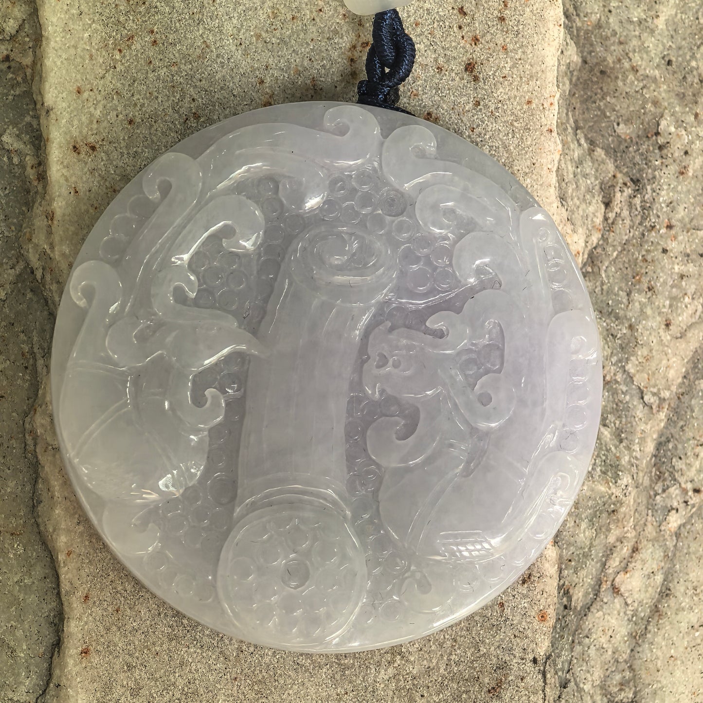 Close-up of carved white jadeite ornament showing raised auspicious patterns and glossy luster.
