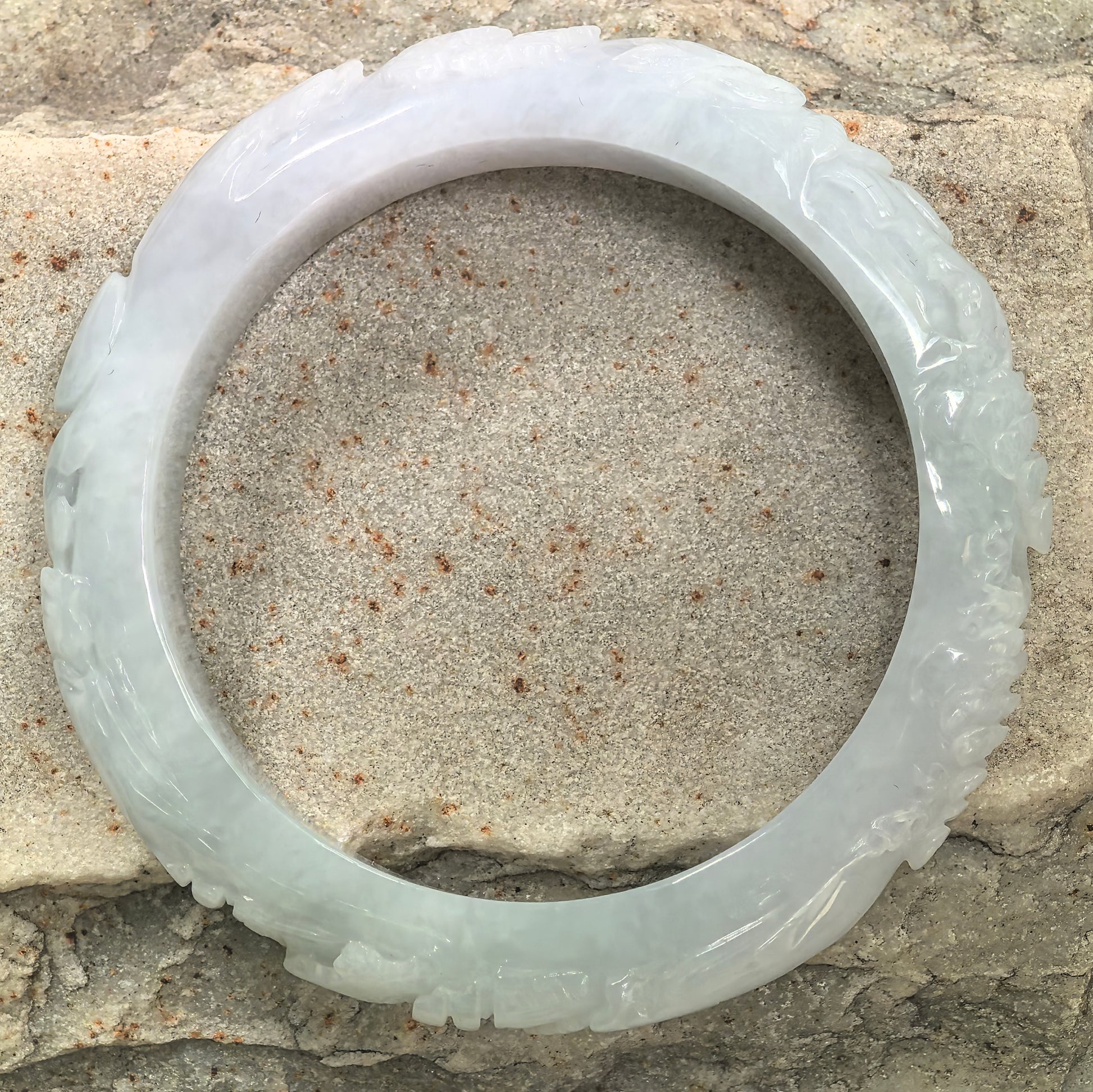 Glutinous white Burmese jadeite bangle with smooth inner side and carved decorative outer profile.
