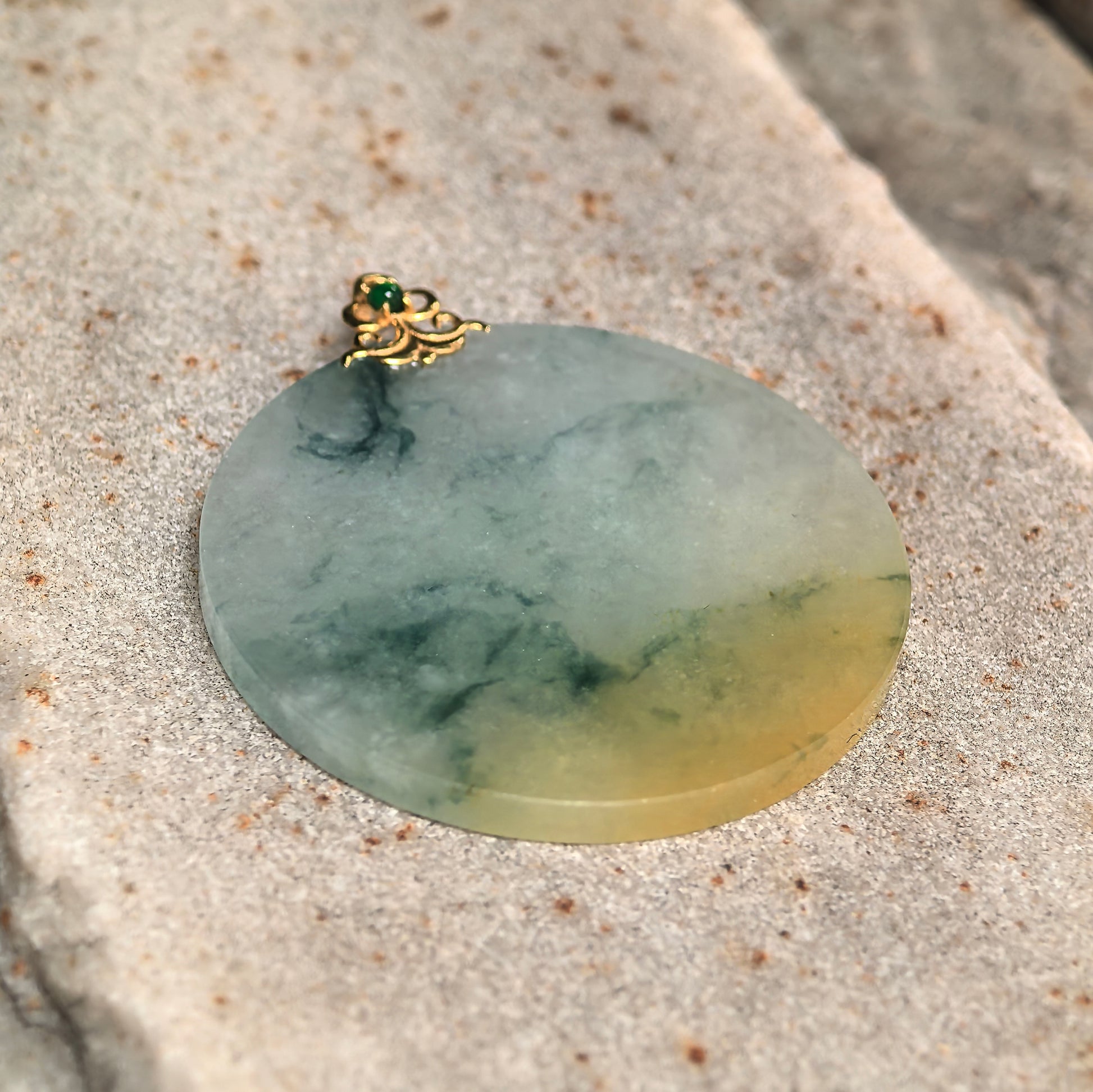 Close-up of yellow-green round jadeite pendant showing soft translucency and natural dark green floating patterns.
