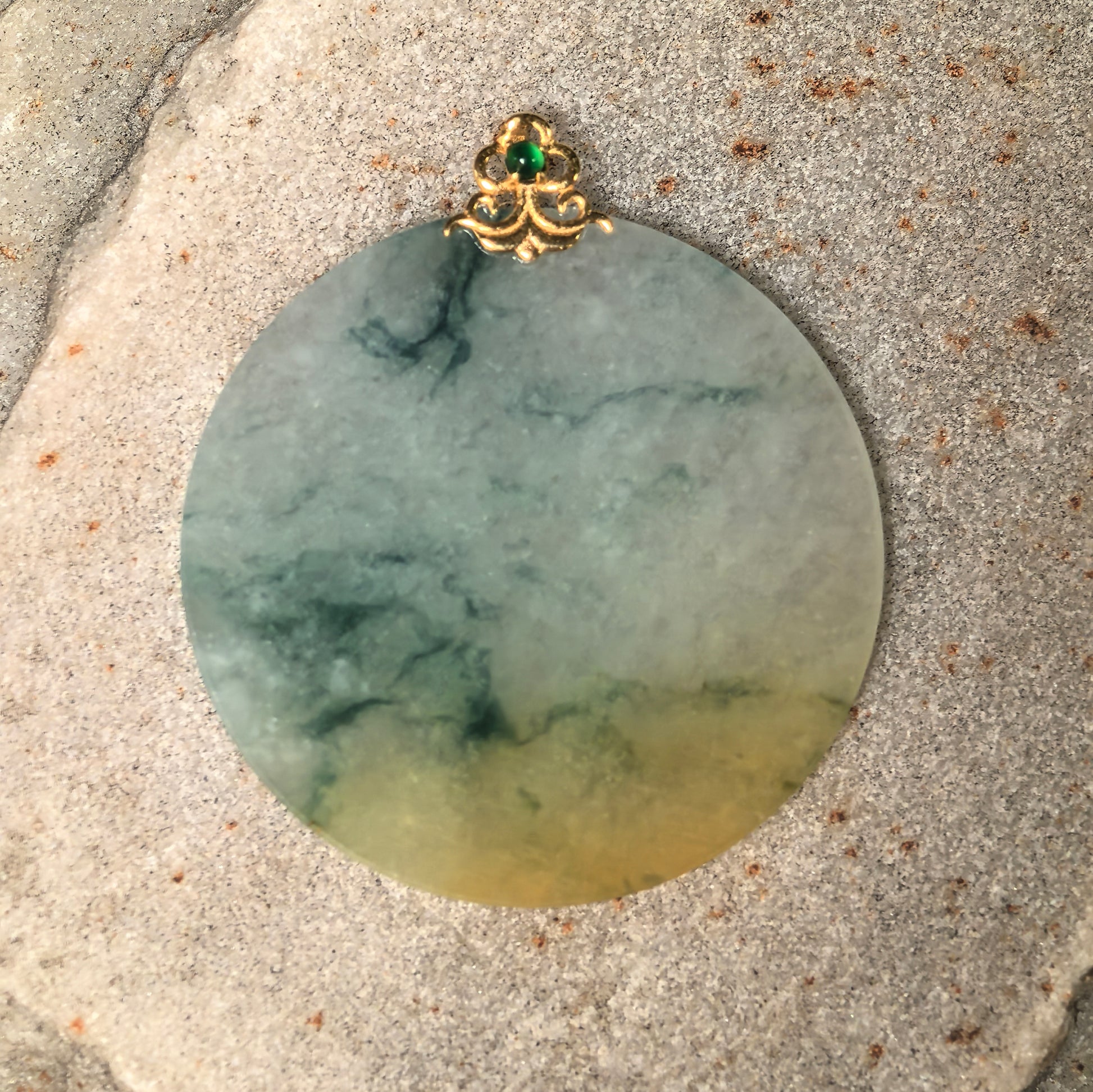 Round plain plaque jadeite pendant displayed on stone with light green and muted yellow color.
