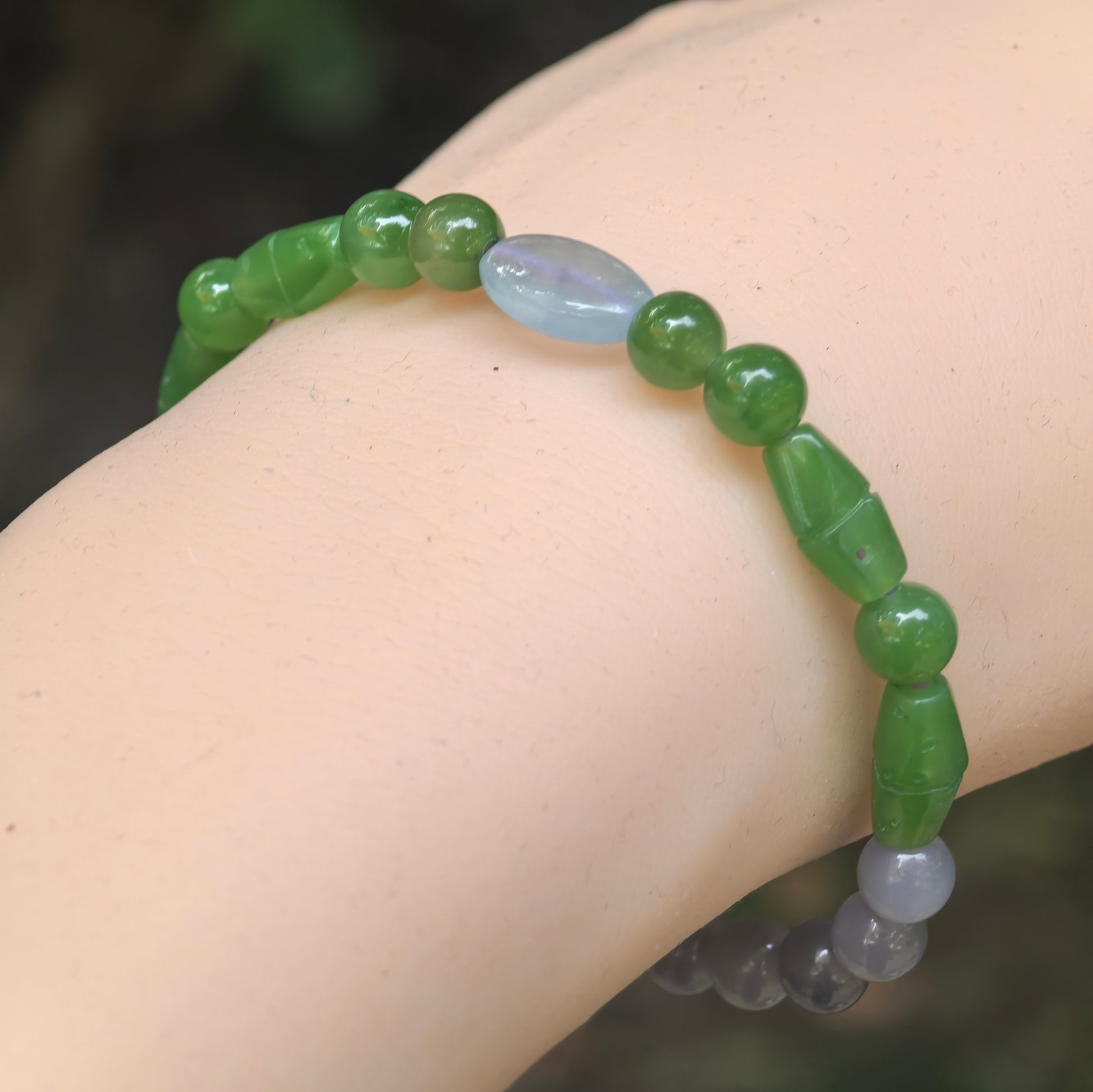 Wrist view of a natural Hetian jade bracelet with deep green carved beads, smoky lavender round beads, and a pale lavender jadeite accent.