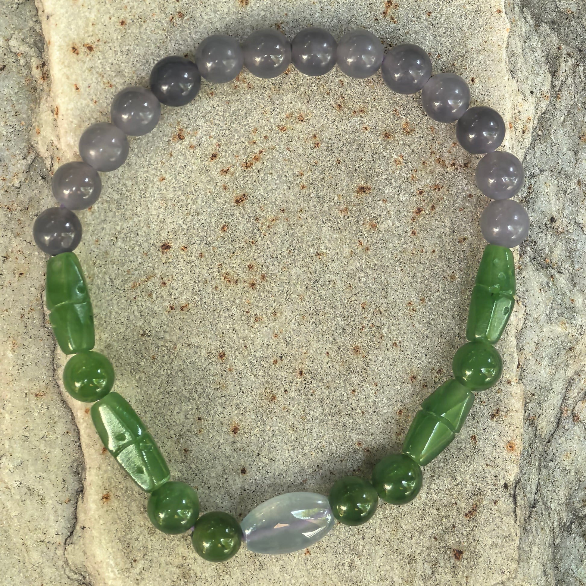 Top-down view of the Hetian jade bracelet showing round smoky lavender beads, green carved beads, and one jadeite accent bead.