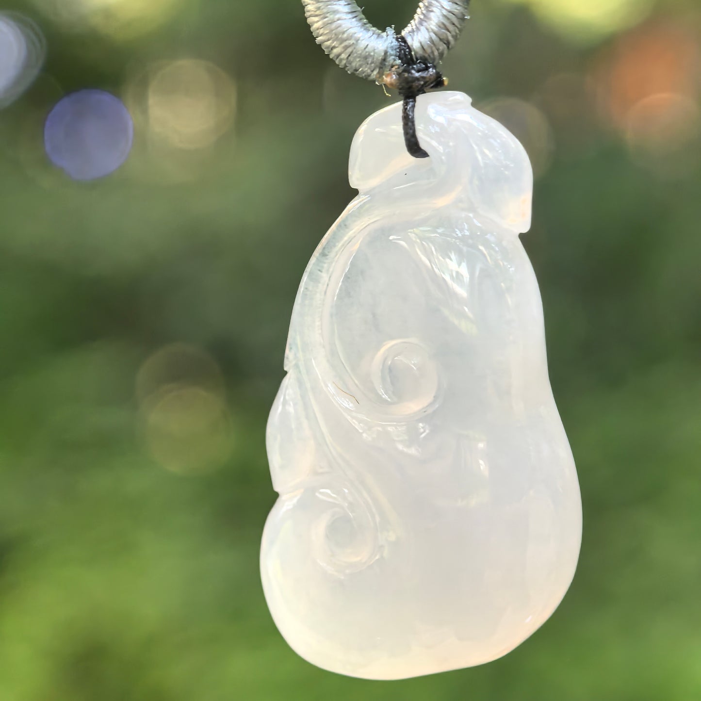 Natural Grade-A icy-glutinous white Ruyi jadeite pendant hanging from a woven cord in natural light.