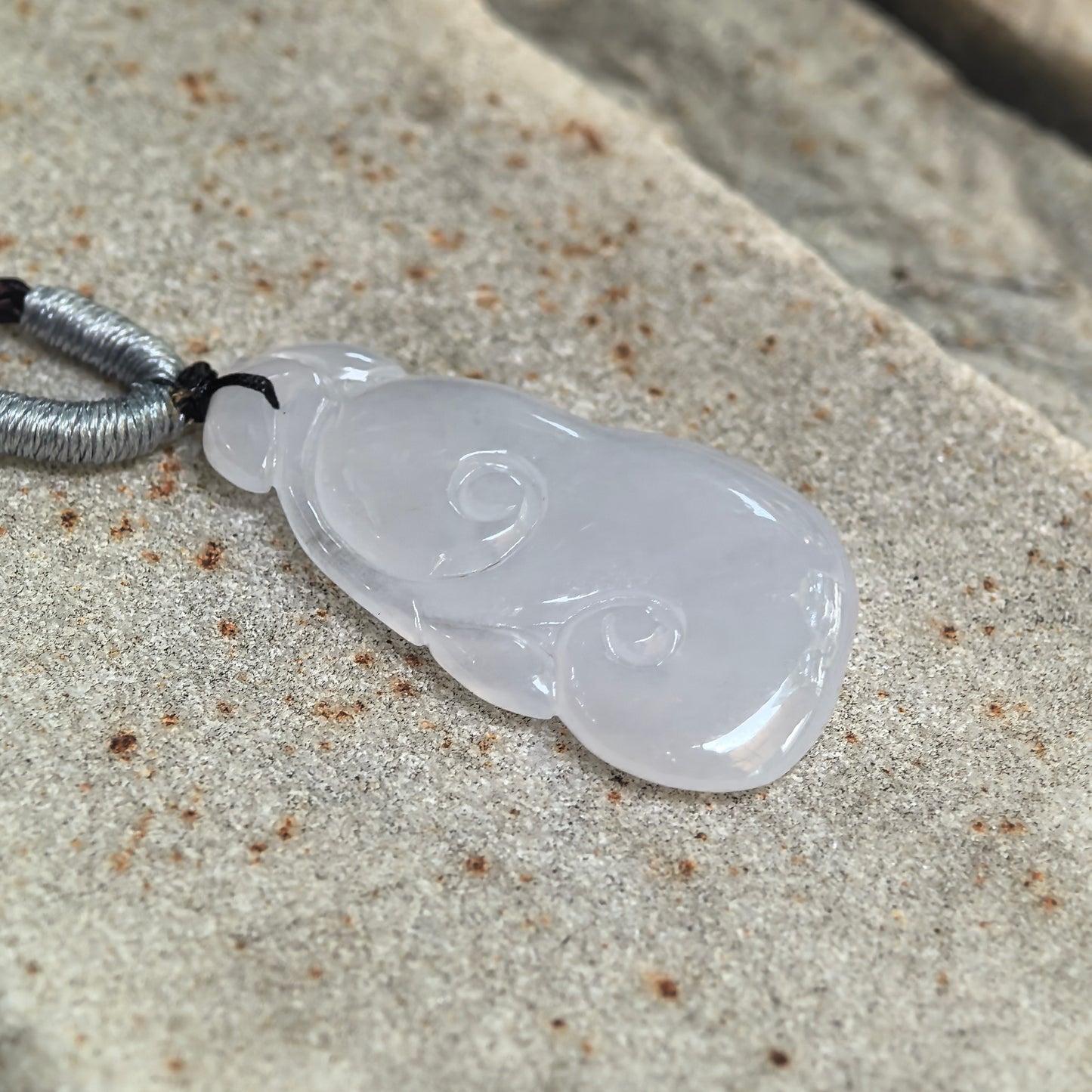 Angled view of a white Burmese jadeite Ruyi pendant showing its translucent icy-gel texture and polished carving.