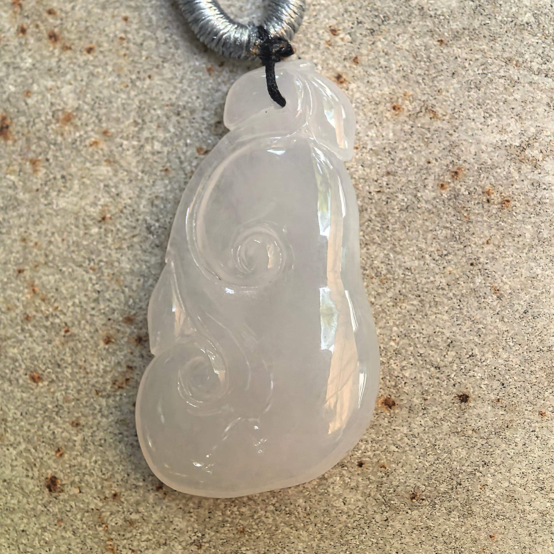 Close-up front view of an icy-glutinous white jadeite Ruyi pendant with flowing scroll details.