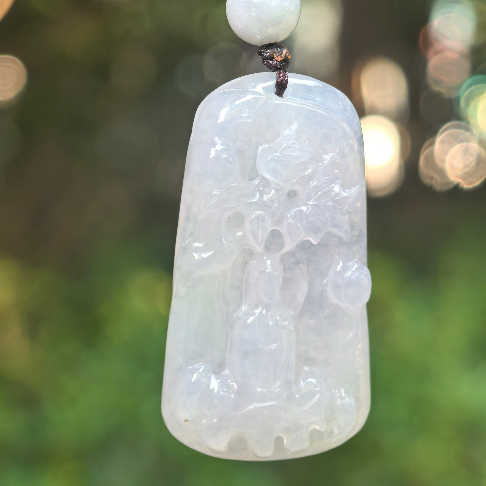 Natural Grade-A icy-glutinous white Guanyin jadeite pendant hanging in natural light with an abstract relief carving.