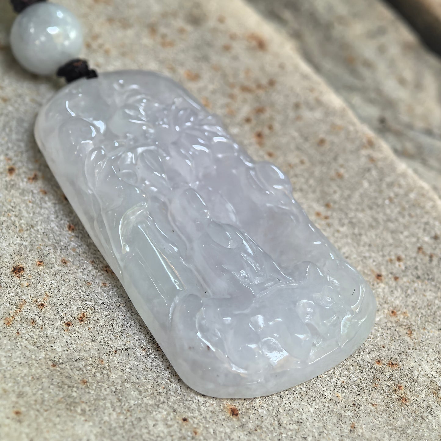 Angled close-up of the white jadeite Guanyin pendant showing its polished surface, translucency, and layered carving.