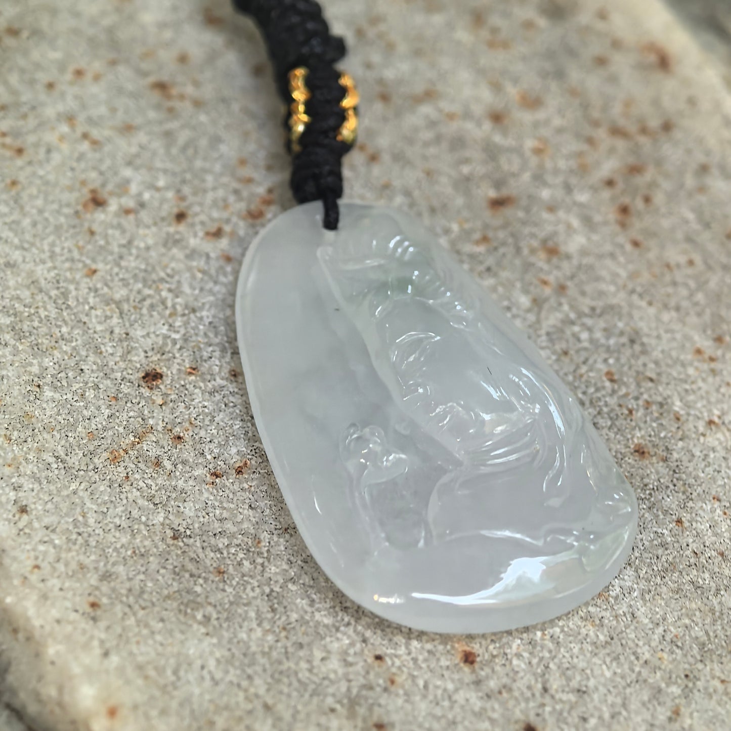 Angled close-up of a white Burmese jadeite Guanyin pendant showing its translucent icy-gel texture and raised carving.