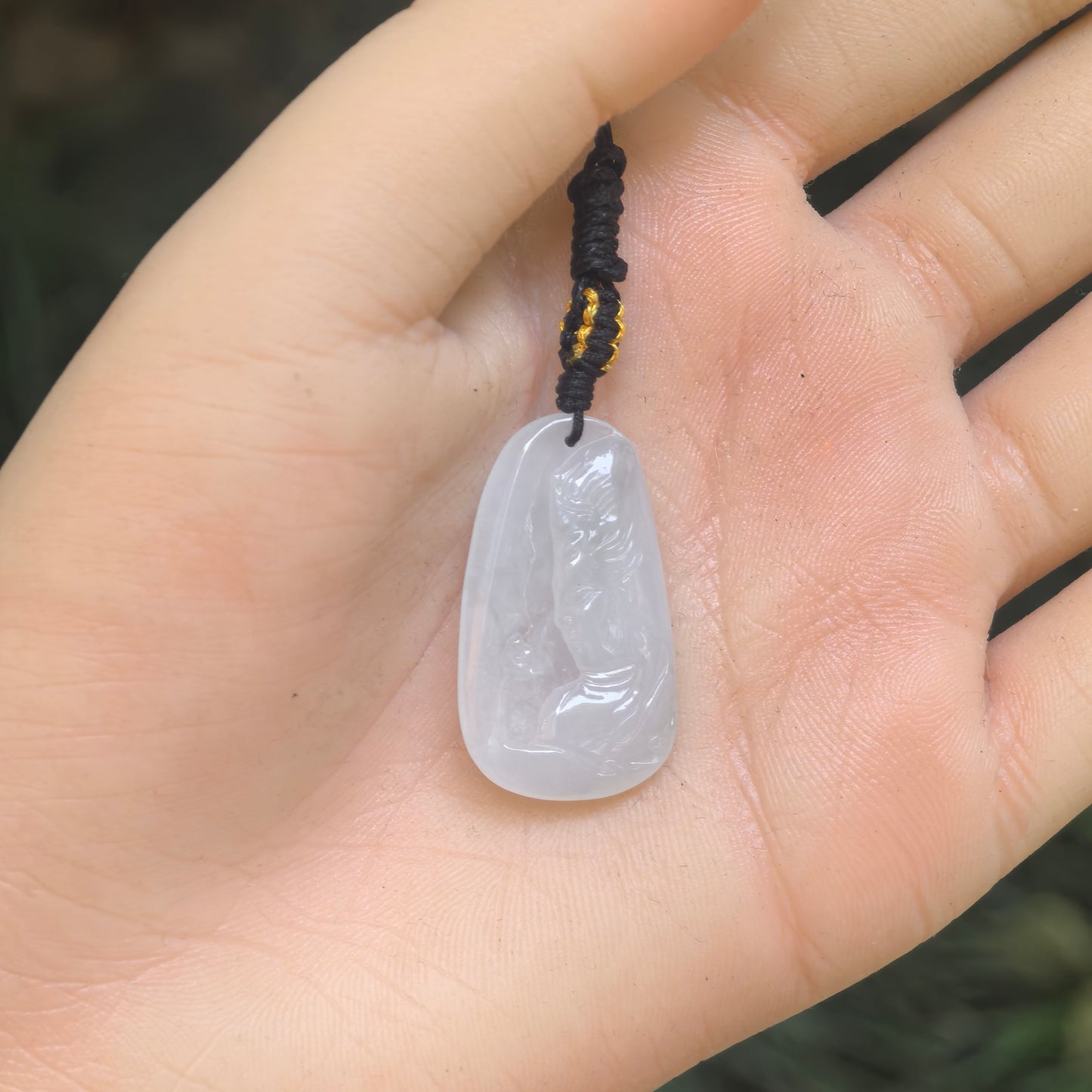 Hand-held view showing the size, rounded shape, and polished finish of the white Guanyin jadeite pendant.