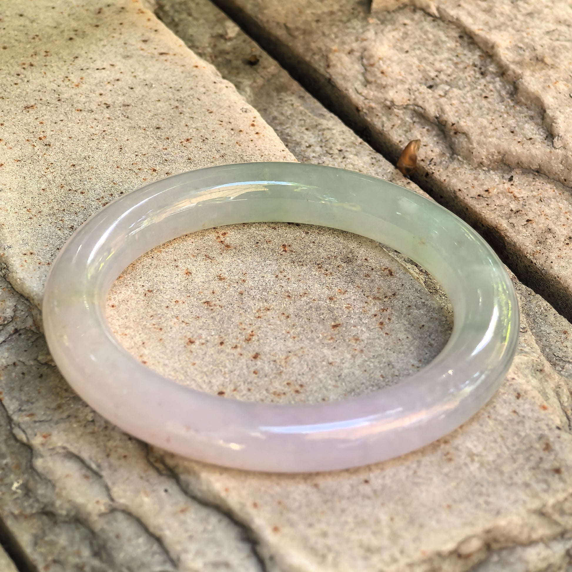 Natural Grade-A lavender and green jadeite round bangle displayed on stone, showing its full rounded profile.