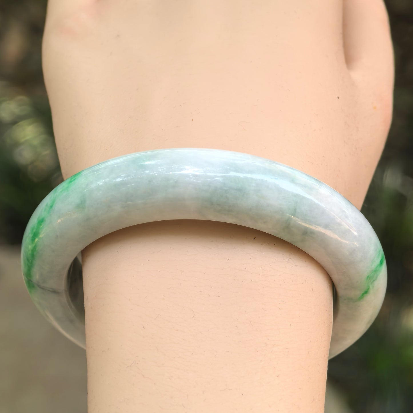 Front wrist view of a green-banded Burmese jadeite D-shape bangle with a broad polished profile.