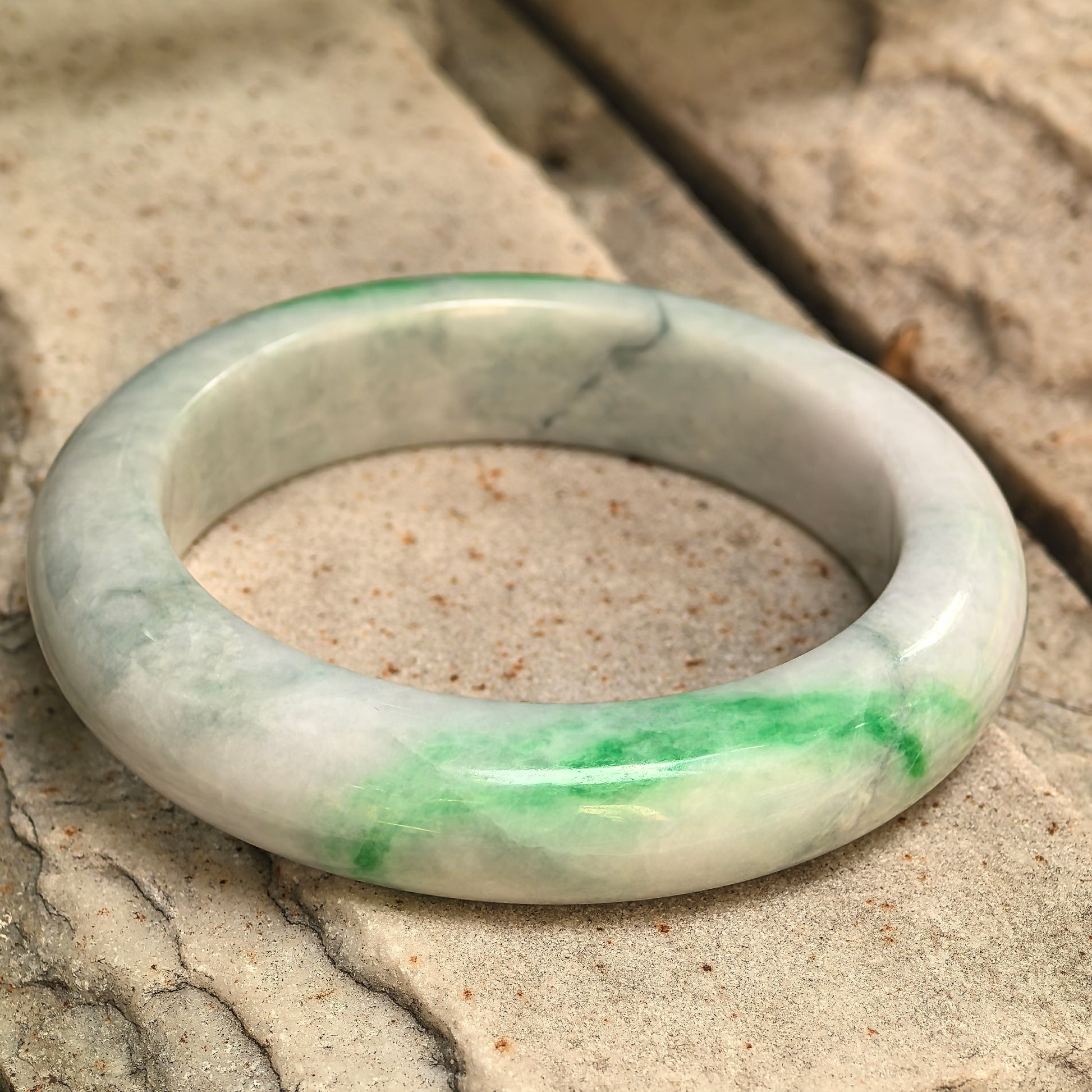 Close-up of a pale green-white jadeite bangle showing vivid green color and visible natural internal lines.