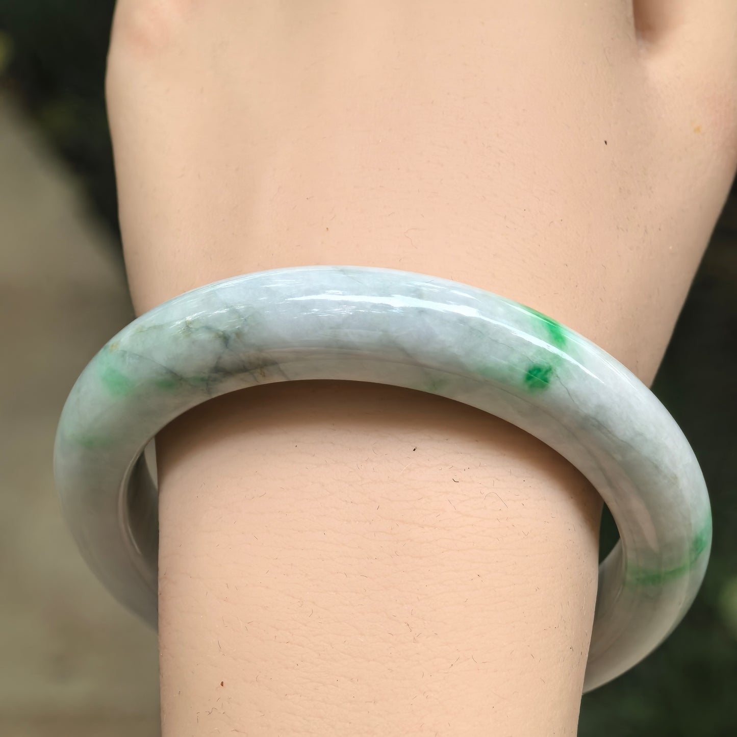 Wrist view of a green-banded Burmese jadeite D-shape bangle showing visible natural internal lines.