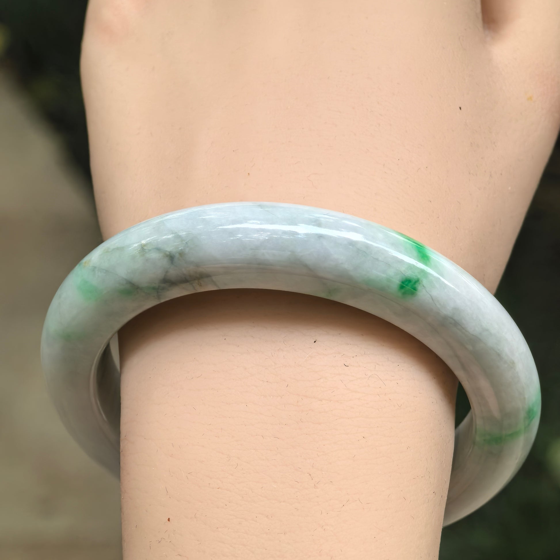 Wrist view of a green-banded Burmese jadeite D-shape bangle showing visible natural internal lines.