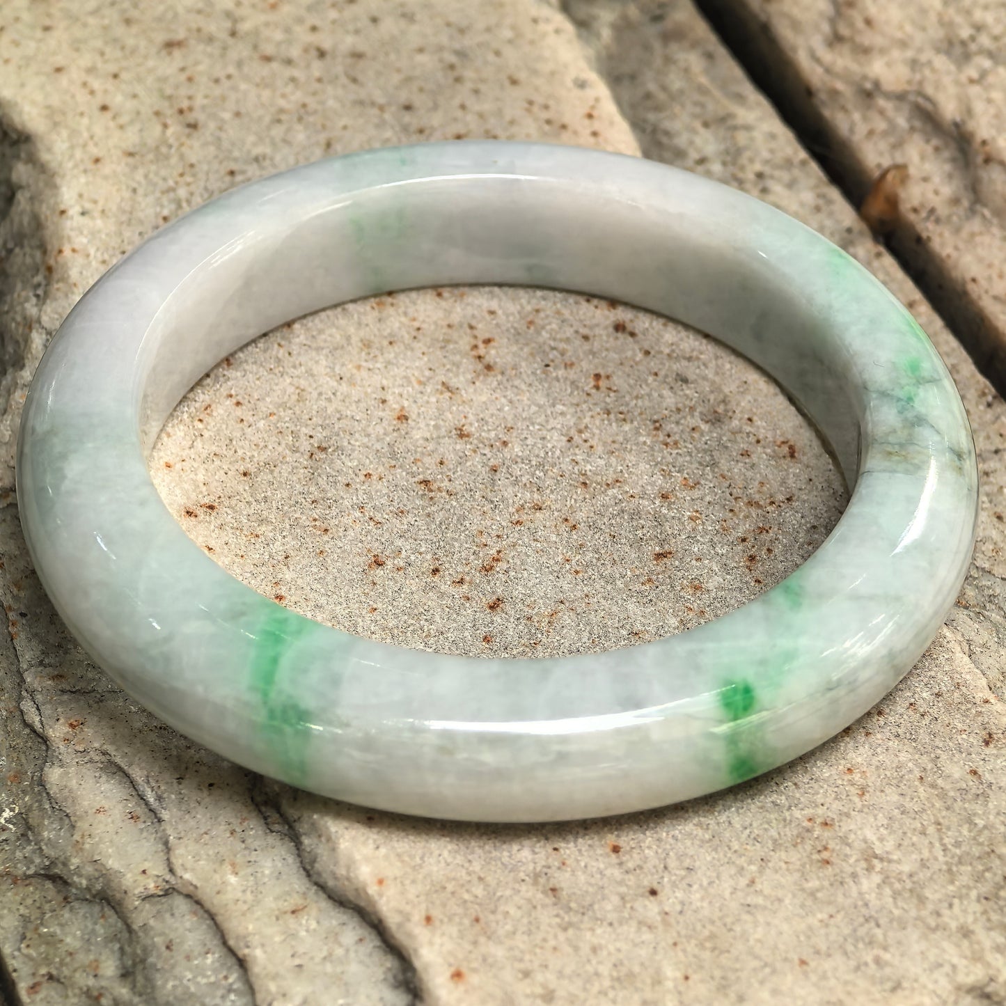 Close-up of a pale green-white jadeite bangle with bright green accents and a smooth polished surface.
