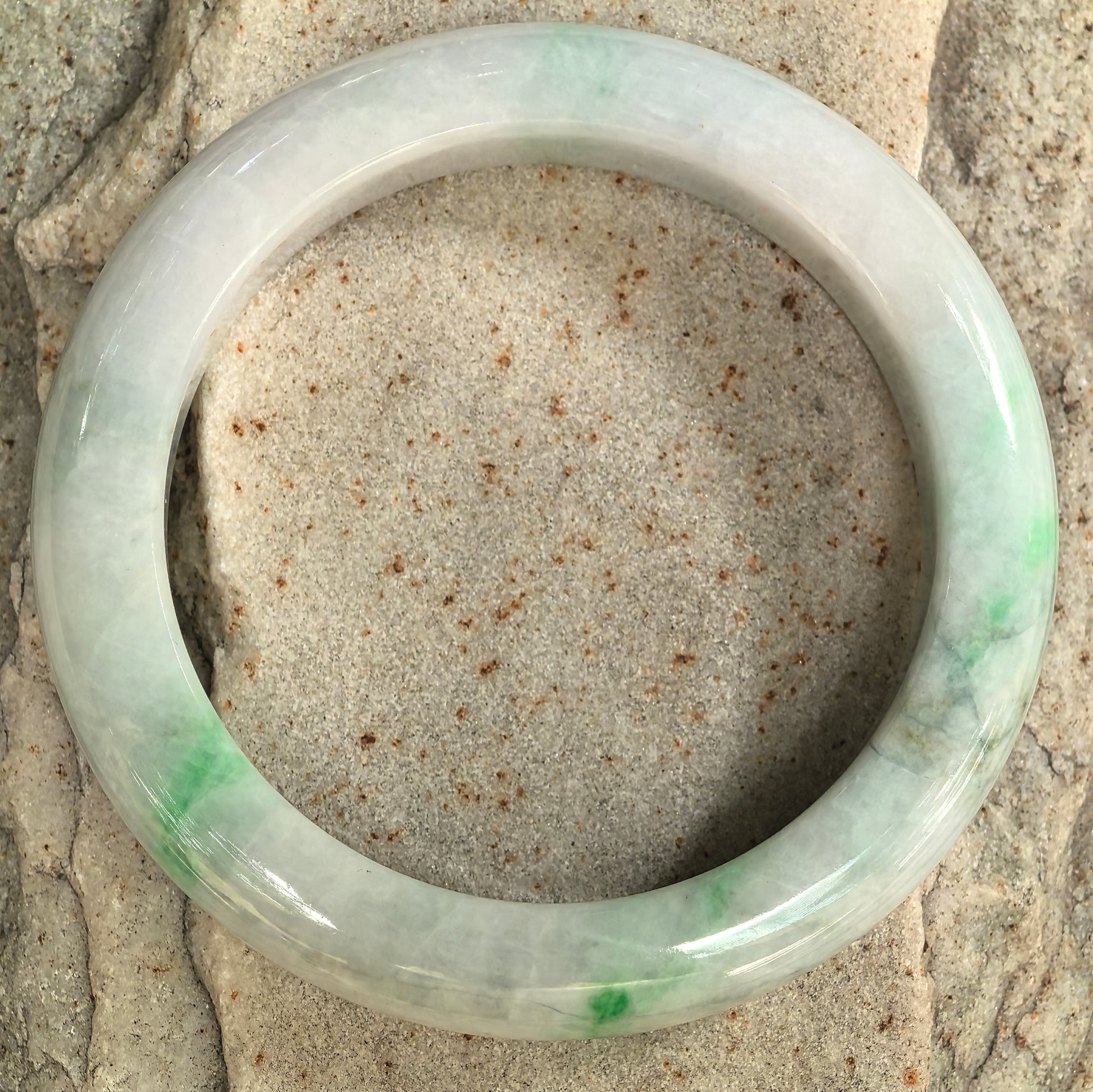 Detailed view of a bean-glutinous green-banded jadeite bangle showing its broad D-shape profile and natural structure.