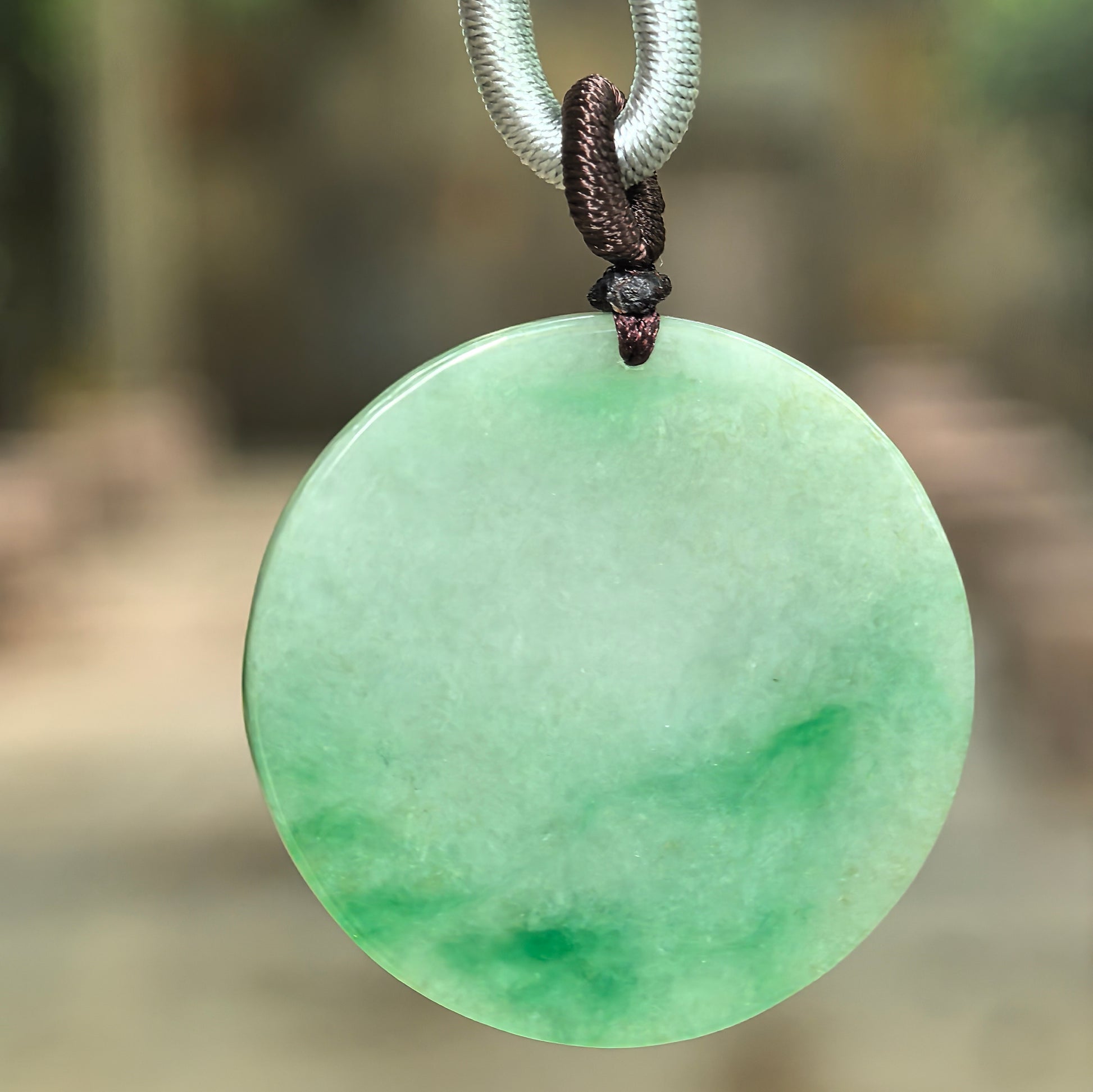 Natural Grade-A glutinous light green jadeite round plain plaque pendant with vivid green floating patterns hanging from its cord.