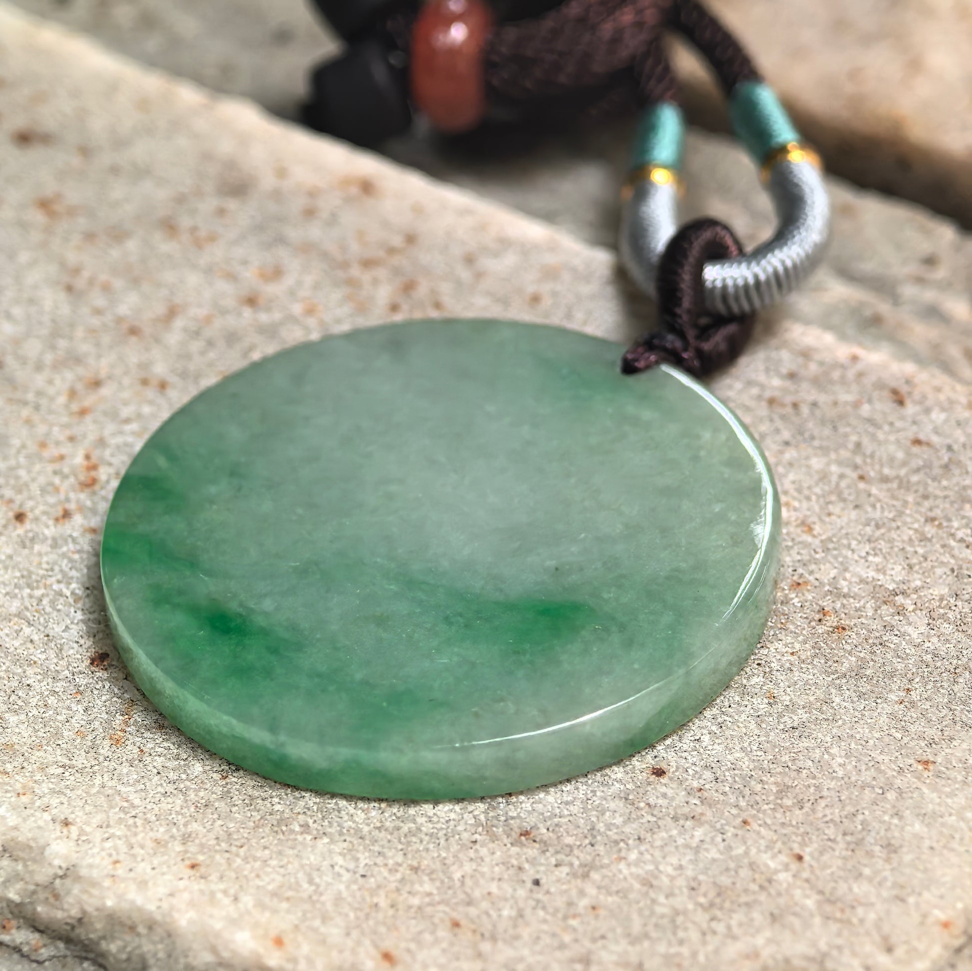 Close-up side view of a glutinous light green jadeite pendant showing its smooth polished edge and even thickness.