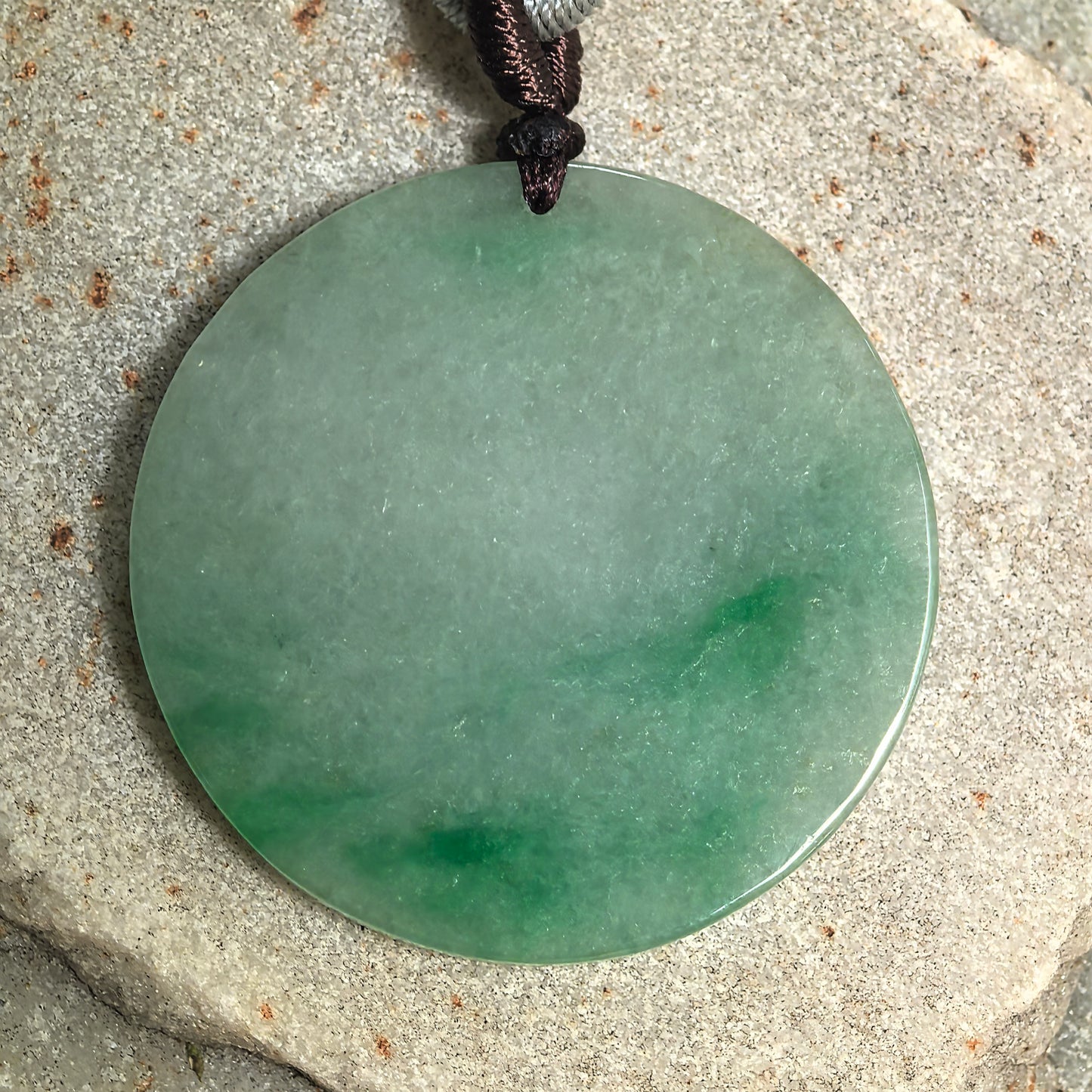Detailed front view of a round jadeite plain plaque pendant with vivid green floating patterns across the lower area.