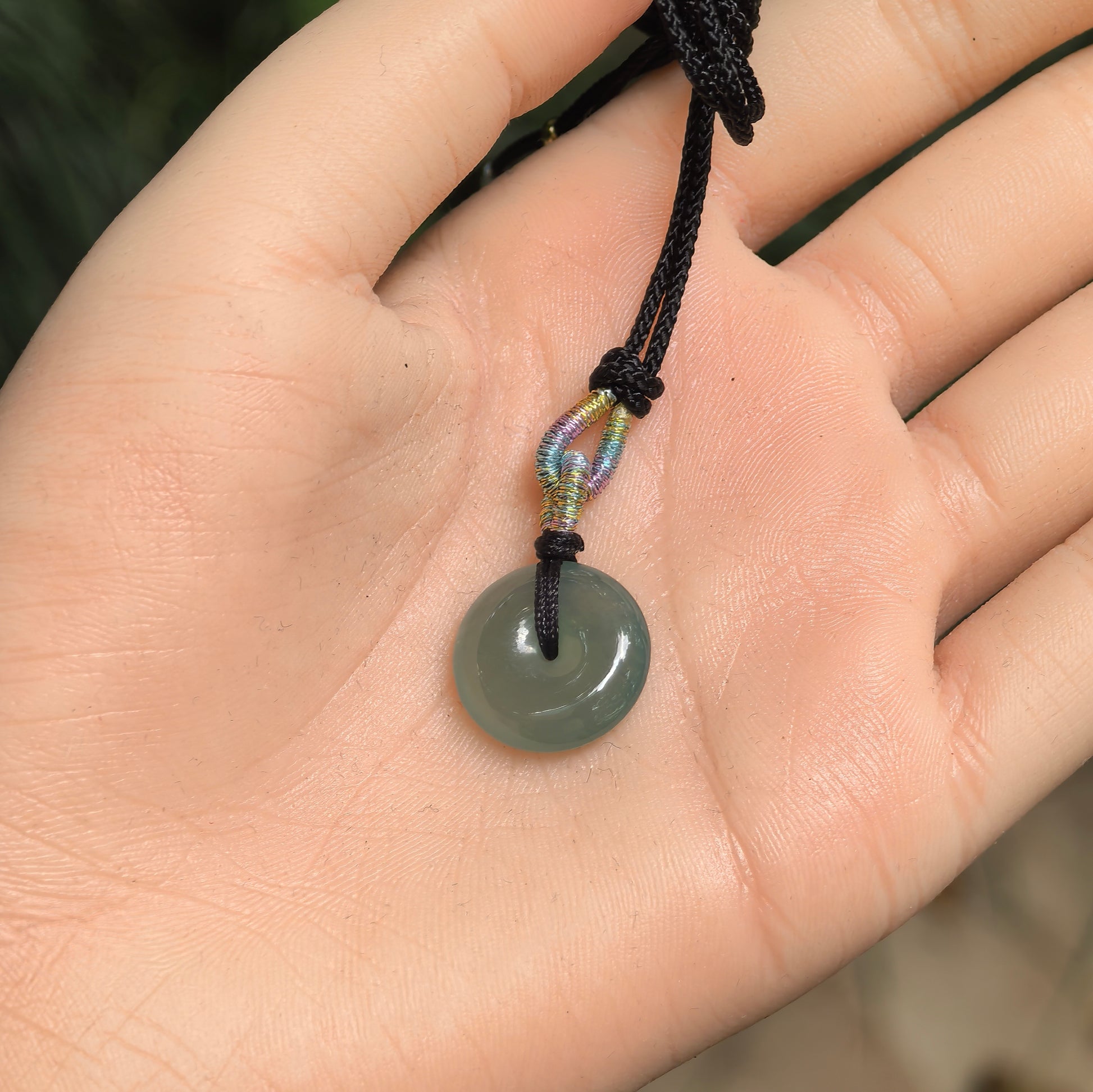 Hand-held view of a petite deep green Burmese jadeite Peace Pendant showing its circular proportions.