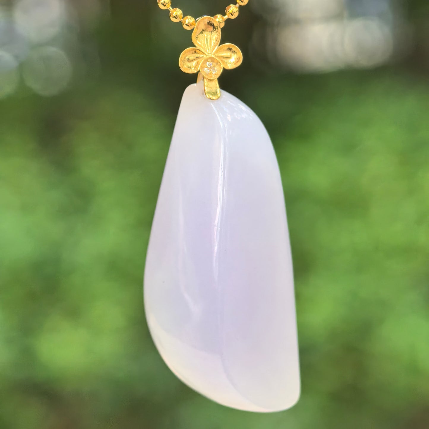 Natural Grade-A icy-glutinous pale lavender freeform jadeite pendant with an 18K gold floral bail hanging in natural light.