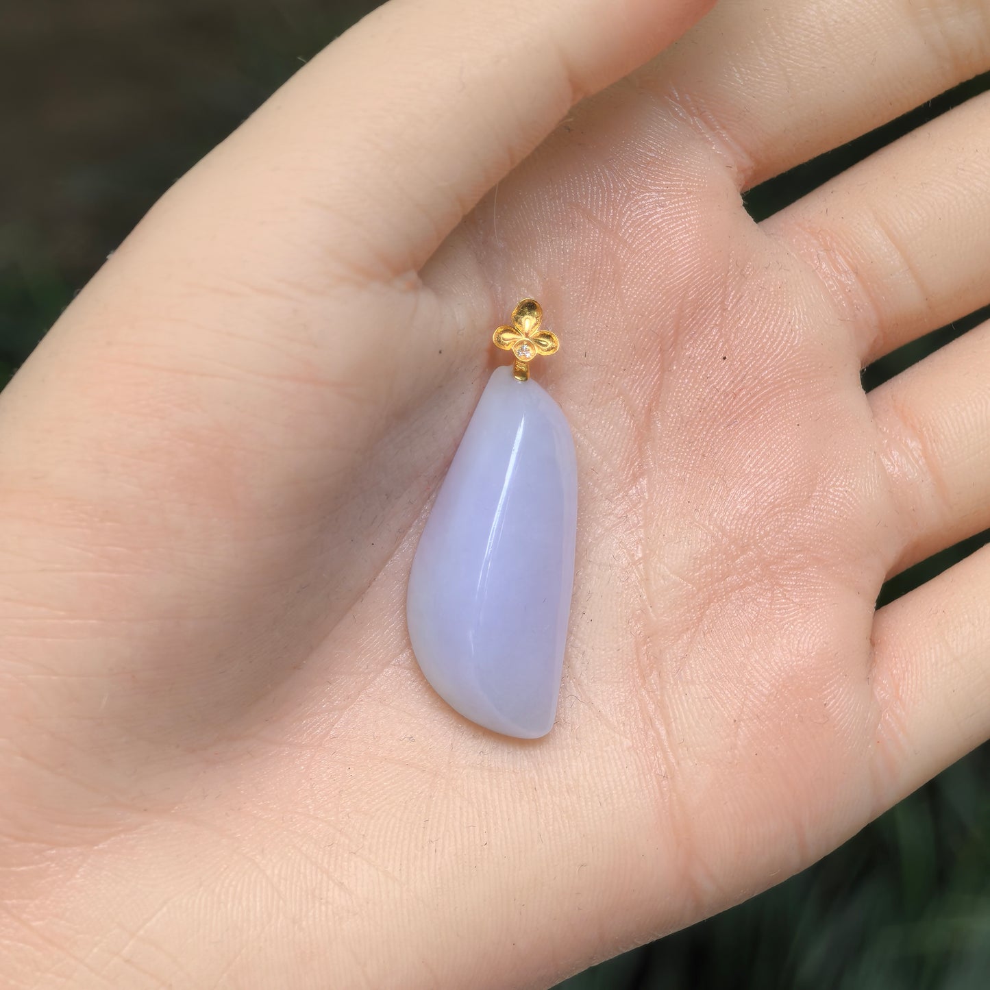 Hand-held view of the pale lavender jadeite pendant showing its curved freeform silhouette and polished surface.