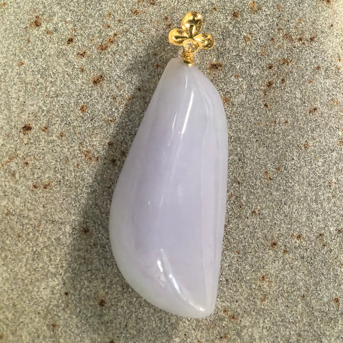 Natural Grade-A pale lavender freeform jadeite pendant displayed flat with its floral 18K gold and diamond bail.