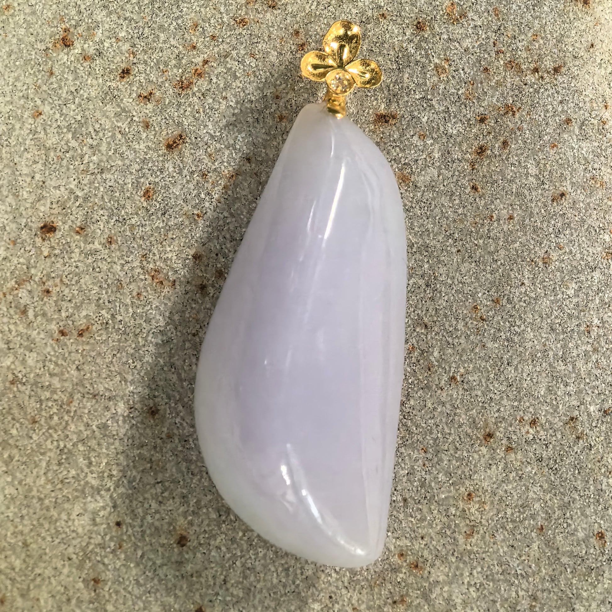 Natural Grade-A pale lavender freeform jadeite pendant displayed flat with its floral 18K gold and diamond bail.