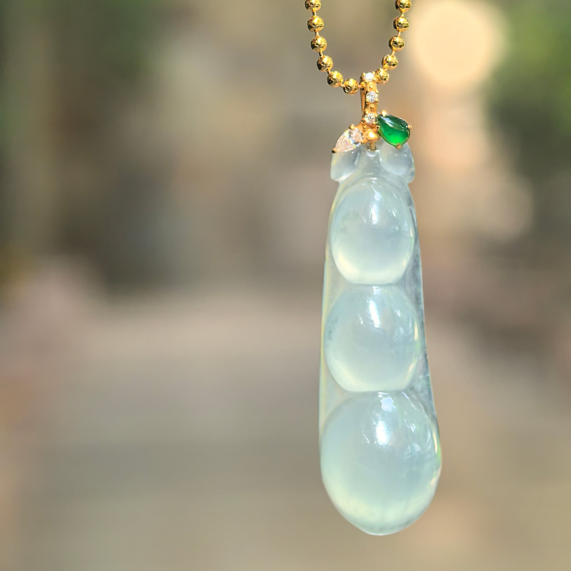 Natural Grade-A icy light green three-bean jadeite pendant with an 18K gold bail hanging in natural light.
