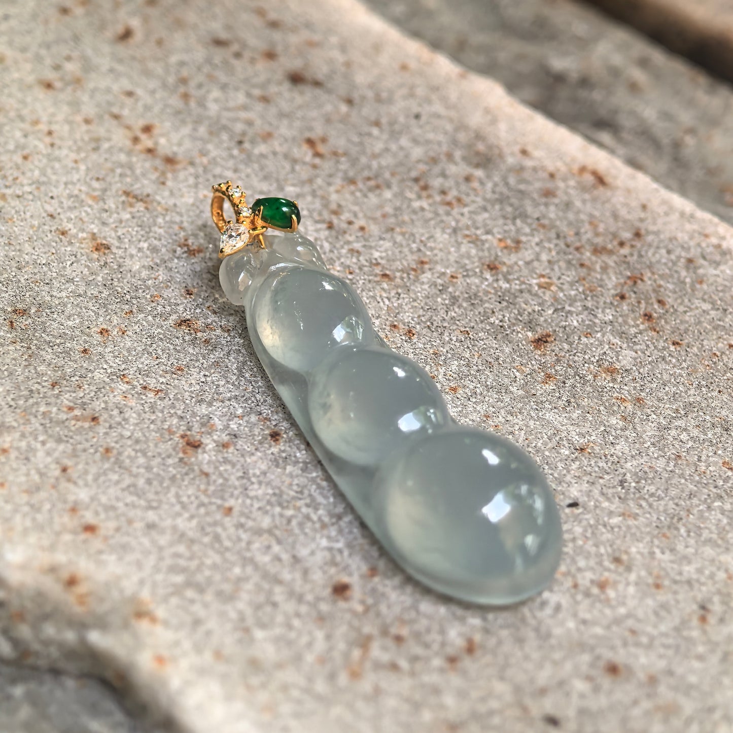 Close-up of the icy light green jadeite bean pendant showing its rounded three-dimensional carving and accent-stone bail.
