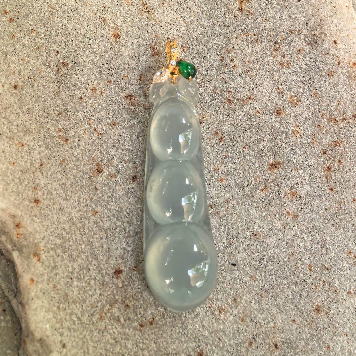 Natural Grade-A light green three-bean jadeite pendant displayed flat, showing its smooth polished surface and glassy luster.