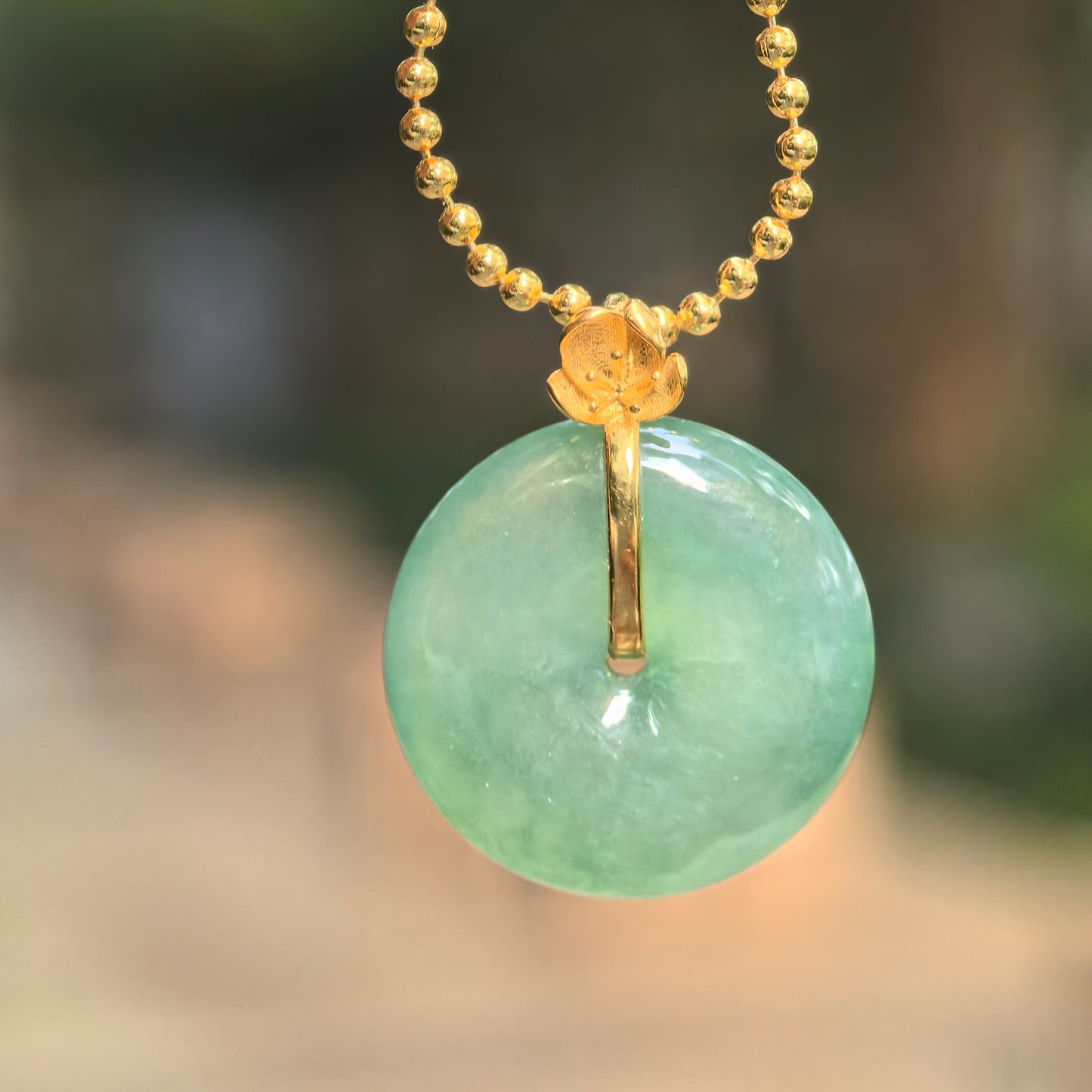 Natural Grade-A icy glutinous light green jadeite Peace Pendant hanging from a gold-tone beaded chain with an 18K gold flower bail.